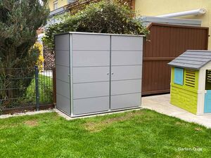 Ein grauer Gartenschrank neben einem Kinderspielhaus im Garten.