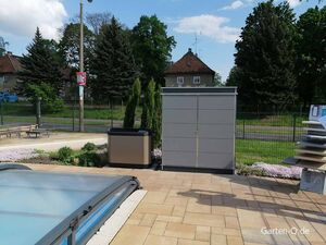 Ein Garten mit Poolabdeckung, modernen Schränken und Pflanzen umgeben von einem Zaun in einer Wohngegend.
