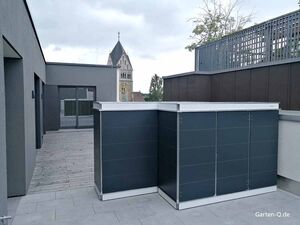 Eine moderne Dachterrasse mit grauen Strukturen, einem Geräteschrank und im Hintergrund eine Kirche.