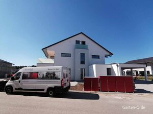 Ein modernes Haus mit einem Lieferwagen von Garten-Q.de und roten Gartenboxen davor.