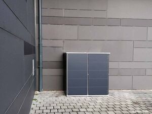 Ein blauer Schrank steht an einer grauen Wand auf einem gepflasterten Boden.