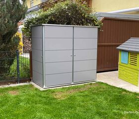 Ein grauer Gartengeräteschrank neben einem Spielhaus in einem kleinen Garten