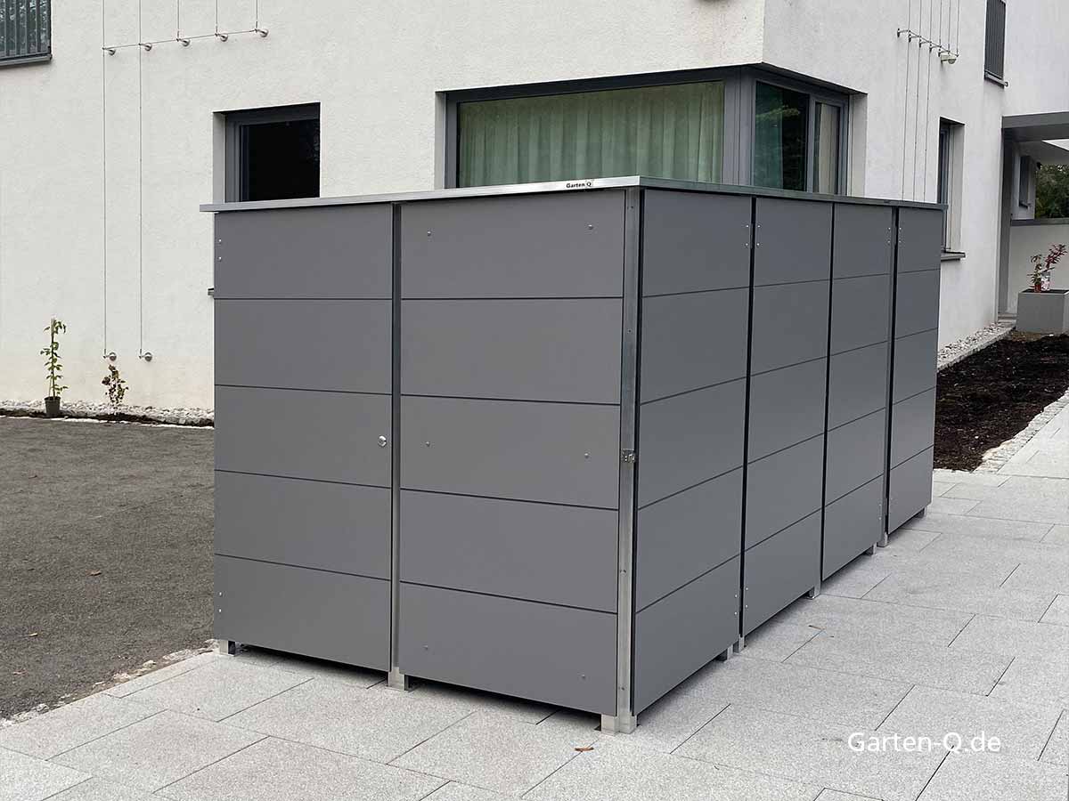 Ein grauer Gartenschrank steht neben einem modernen Gebäude auf einer gepflasterten Fläche.